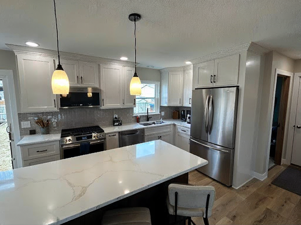 Modern kitchen with white cabinets, stainless steel appliances, marble island, pendant lights, and wooden flooring—perfect for those considering cabinet refinishing or upgrading their kitchen cabinets.