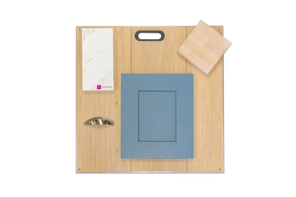 A sample board for the Showroom displays a marble countertop piece, a light wood square, a blue cabinet door, and a metallic cup handle, all arranged on a wooden panel.