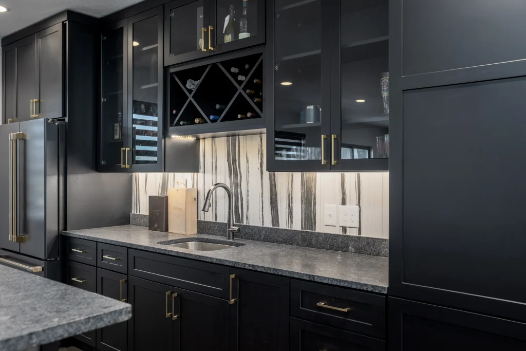 Modern kitchen with black cabinets, gold handles, a marble backsplash, under-cabinet lighting, a wine rack, and a stainless steel sink with a gray countertop—offering custom comfort far beyond builder grade finishes.