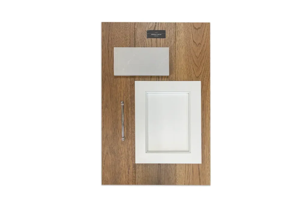 A sample board for the showroom displays a wood panel background, a rectangular metal handle, a white cabinet door front, and a light gray countertop material sample.