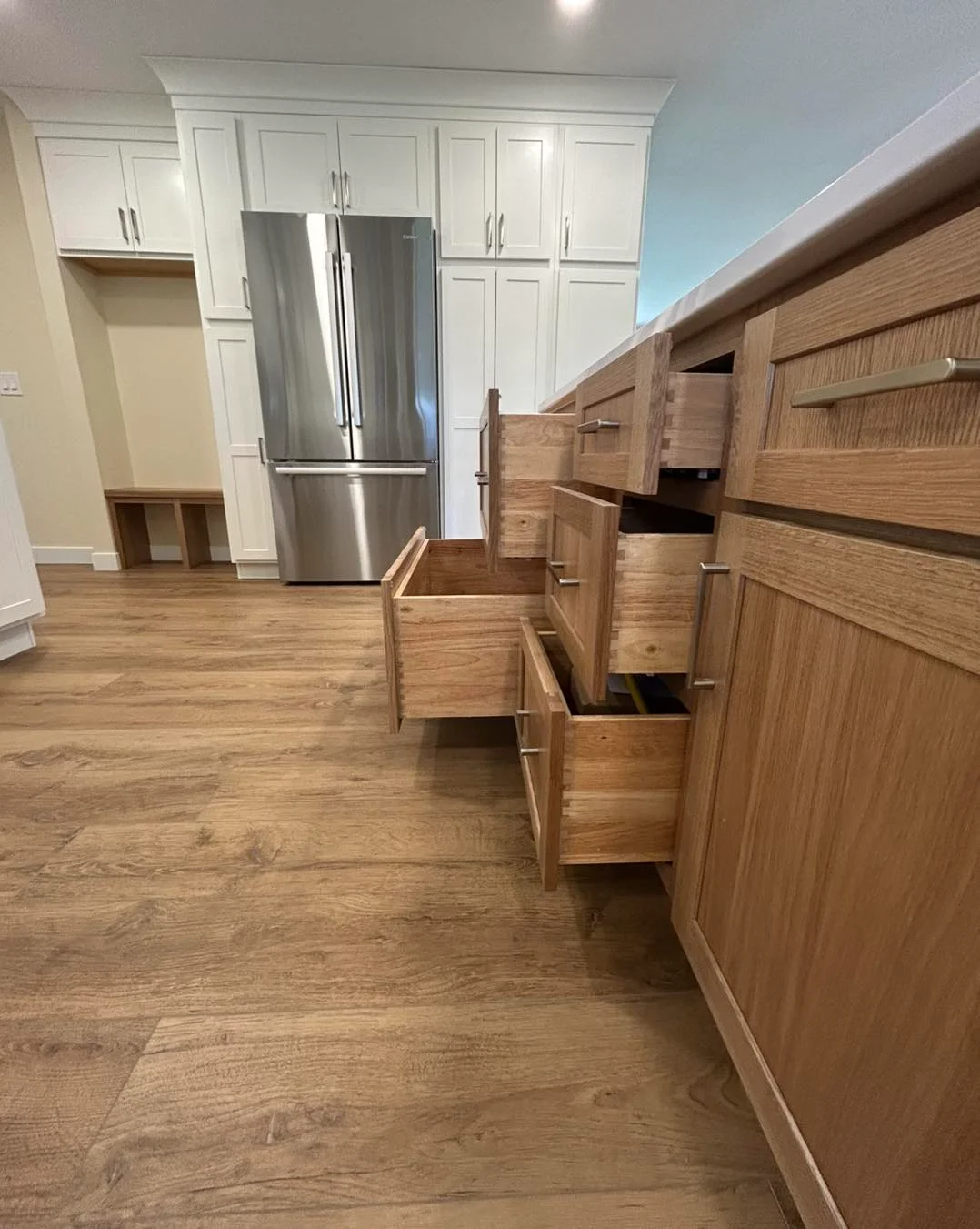 Several wooden kitchen drawers and cabinets are open, revealing empty interiors; a stainless steel refrigerator and white cabinets are in the background, showcasing a recent Kitchen Remodel in Milan IL.