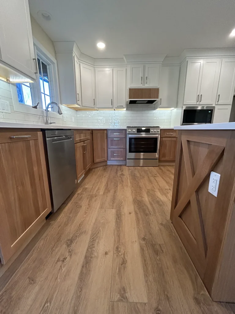 Modern kitchen remodel in Milan IL featuring wood and white cabinets, stainless steel appliances, light wood flooring, and a white tile backsplash.