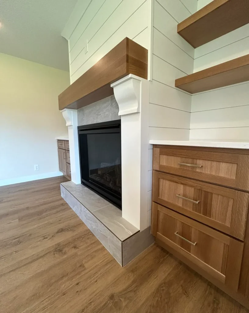 A modern living room in Milan IL features a fireplace with a wood mantel, white shiplap walls, built-in shelves, and wood cabinetry on a hardwood floor—perfect inspiration for your next kitchen remodel.