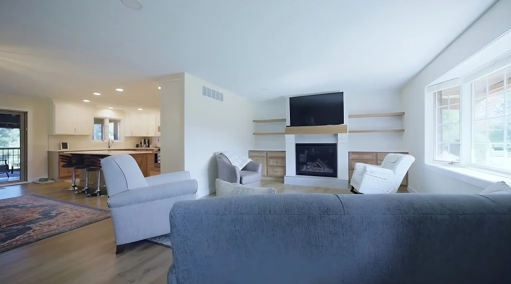 Bright living room with a gray sofa, two armchairs, built-in shelves, a fireplace, and a wall-mounted TV; kitchen remodel visible in the background of this Milan IL home.