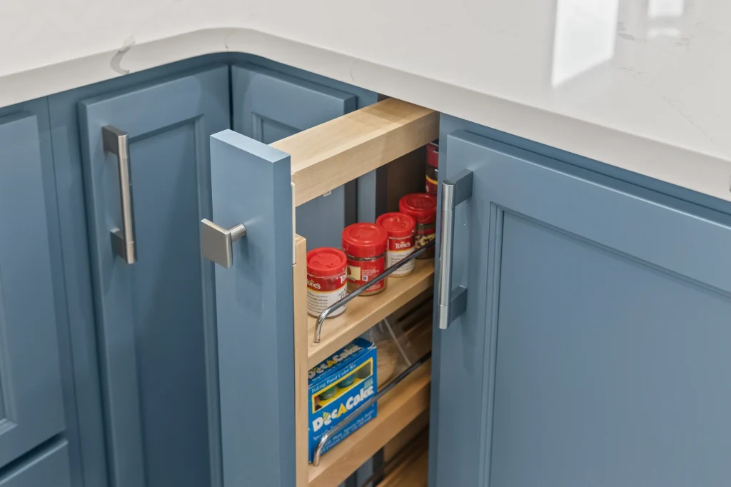 A pull-out pantry drawer in a blue kitchen cabinet holds spice jars and food storage bags under a white countertop.