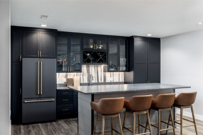Modern home kitchen with dark cabinets, a built-in fridge, wine storage, marble backsplash, and a large island with four brown leather barstools.