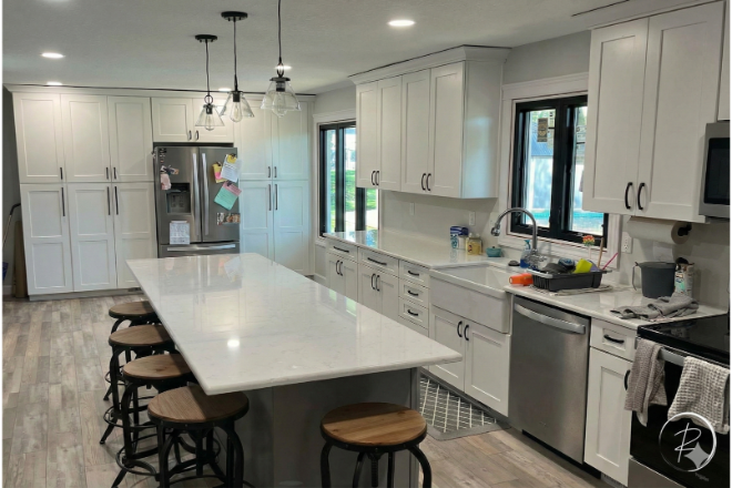 Modern kitchen with white cabinets, a long marble island with stools, stainless steel appliances, and large windows above the sink. Modern kitchen with white cabinets, a long marble island with stools, stainless steel appliances, and large windows above the sink.