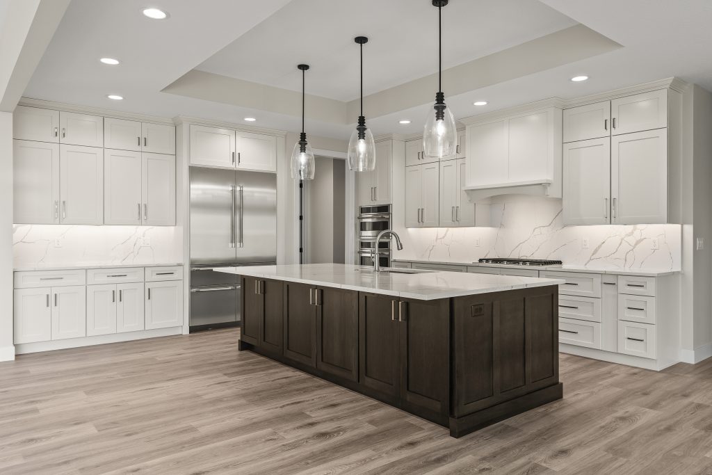 Modern kitchen with white cabinets, marble backsplash, and a dark wood island beneath three pendant lights as a focal point.