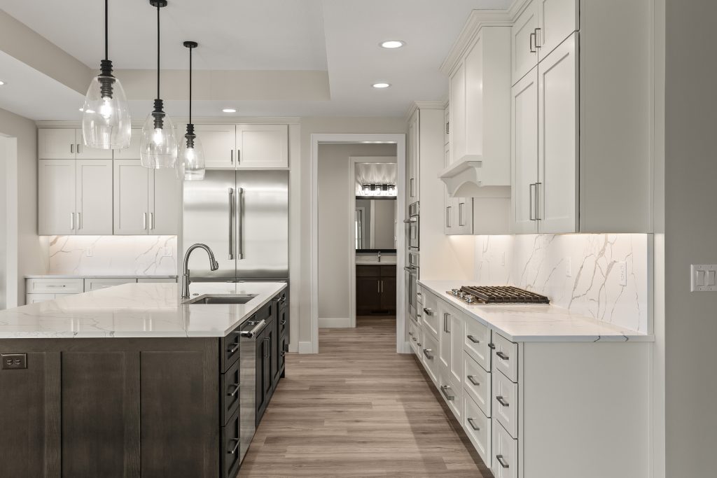 Bright modern kitchen with white cabinets, marble countertops, and a large island with a sink and pendant lights over it.