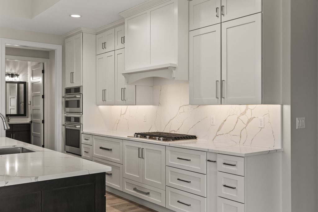 White kitchen with marble backsplash and countertops, built-in ovens, and a gas cooktop.