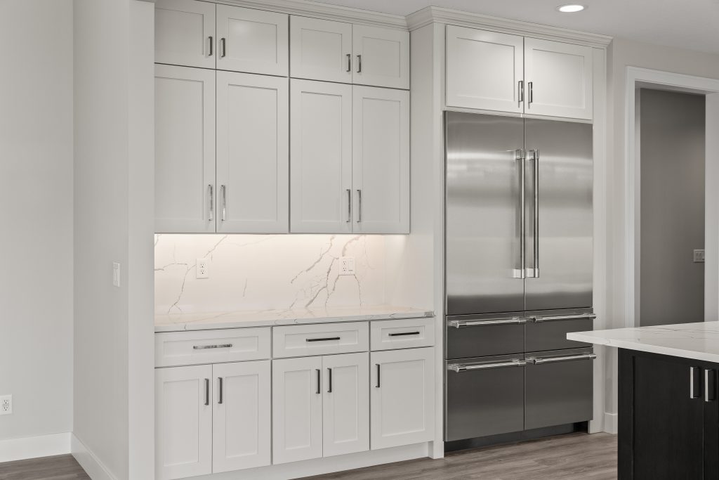 Modern kitchen with white shaker cabinets, marble backsplash, and a stainless steel French‑door refrigerator.