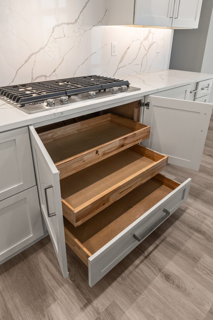 Open white kitchen with a stainless gas range and marble backsplash; bottom drawers pulled out showing wood interiors.