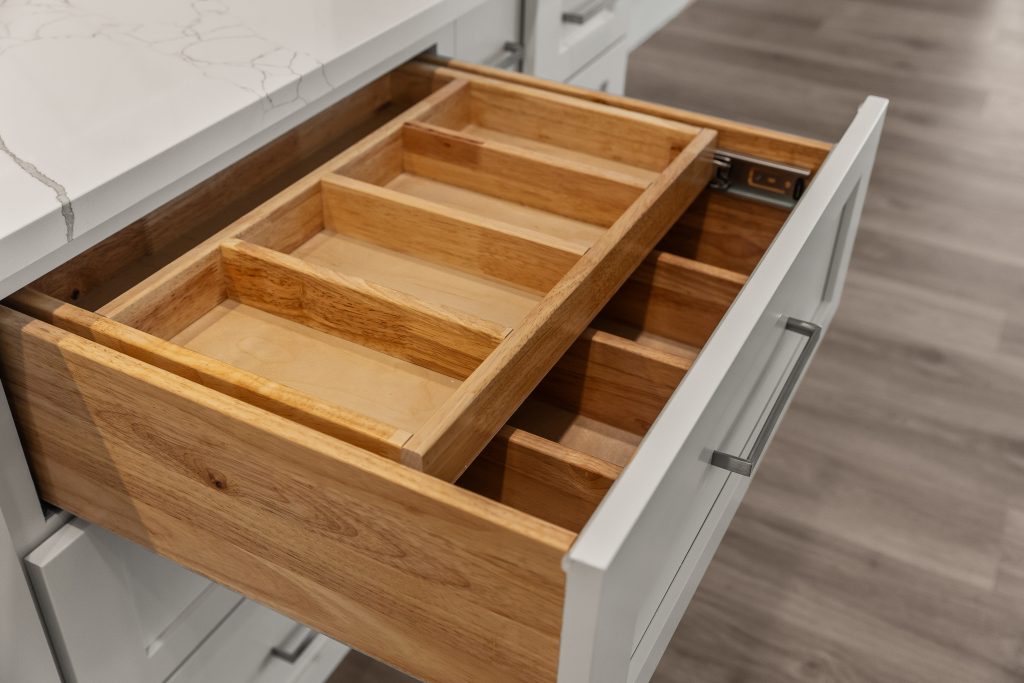 Open kitchen drawer with oak utensil organizers and multiple compartments visible in a modern white cabinet.