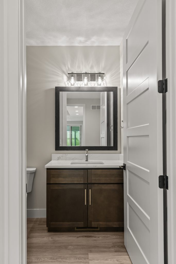 Modern bathroom vanity with a dark wood cabinet, white marble countertop, and a large black-framed mirror above the sink. A four-bulb fixture provides lighting.