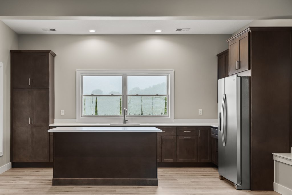 Modern kitchen with dark wood cabinets, stainless steel refrigerator, and a central island under a window