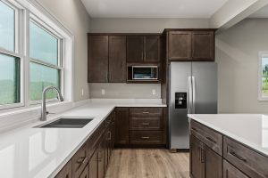 U-shaped kitchen with dark wood cabinets, white countertops, a stainless steel refrigerator and microwave, and a window above the sink by the left wall.