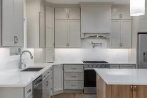 Modern gray kitchen with white marble countertops, stainless steel appliances, and an island with wood base.