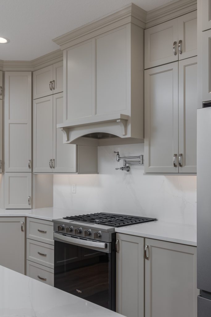 Modern kitchen with light gray cabinets, marble-like white backsplash, and a stainless steel gas range.