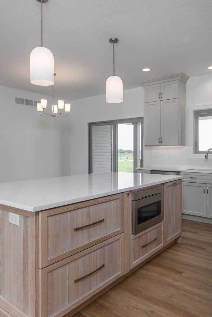 Modern kitchen with a white quartz island, wood base cabinets, stainless microwave, and white upper cabinets with pendant lights.