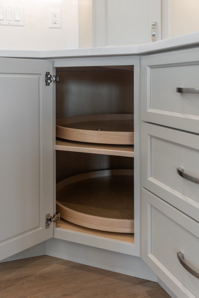 Open corner kitchen cabinet with circular wooden lazy Susan shelves inside, white cabinetry visible.