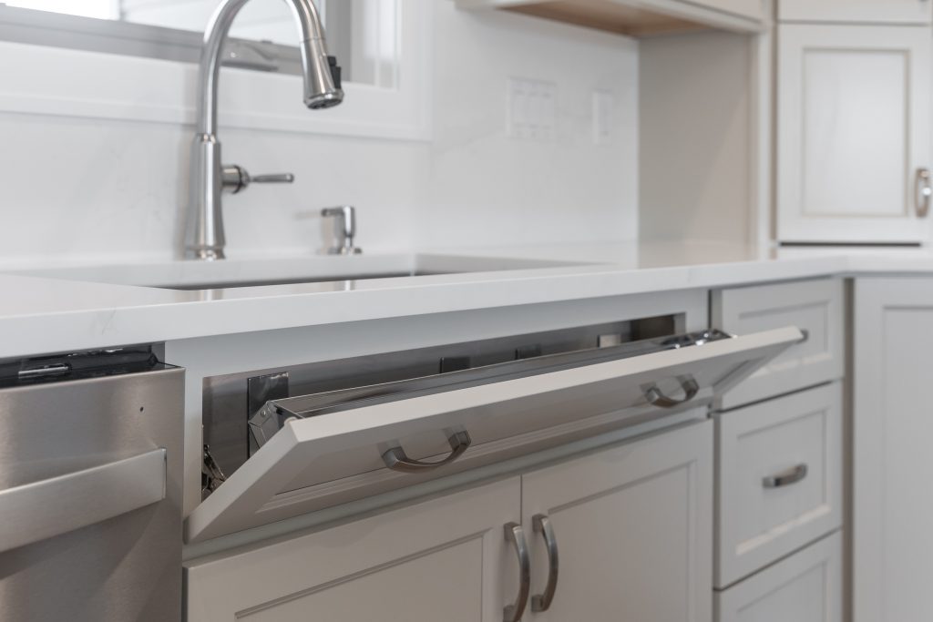 Open dishwasher drawer in a clean white kitchen with a stainless steel faucet above it.