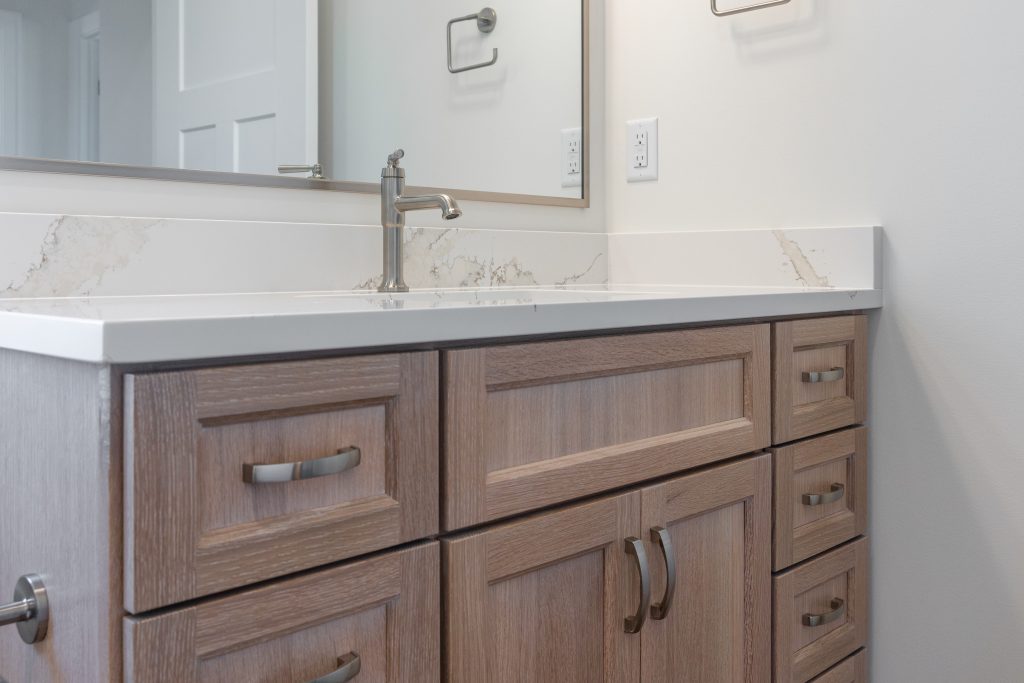 Bathroom vanity with marble countertop, chrome faucet, and wooden cabinets beneath a large mirror