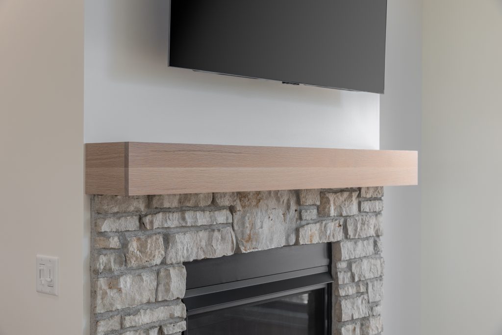 Stone fireplace with a light wood mantle and a mounted flat-screen TV above.