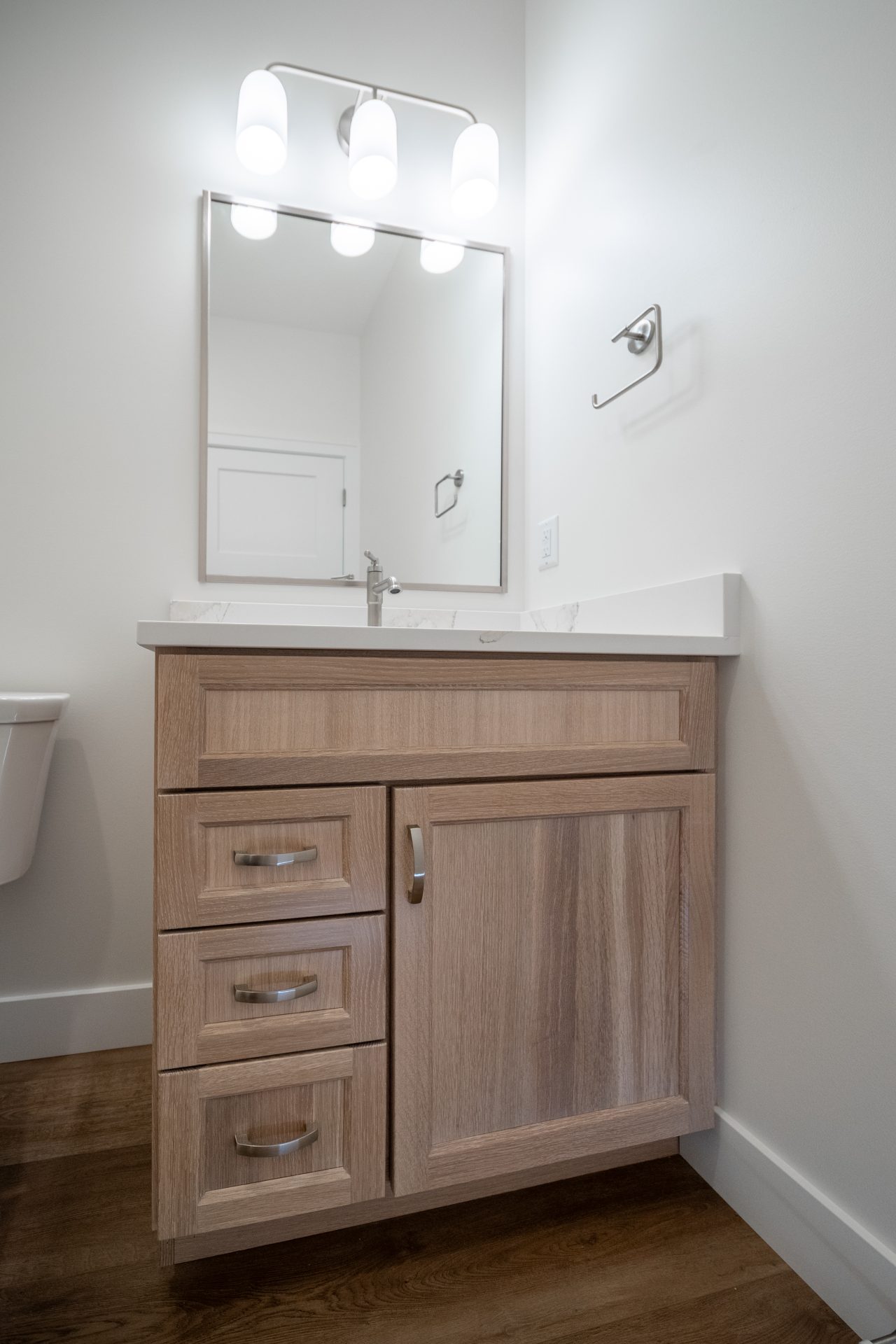 Wood vanity with drawers and a marble countertop beneath a rectangular mirror in a bright bathroom.