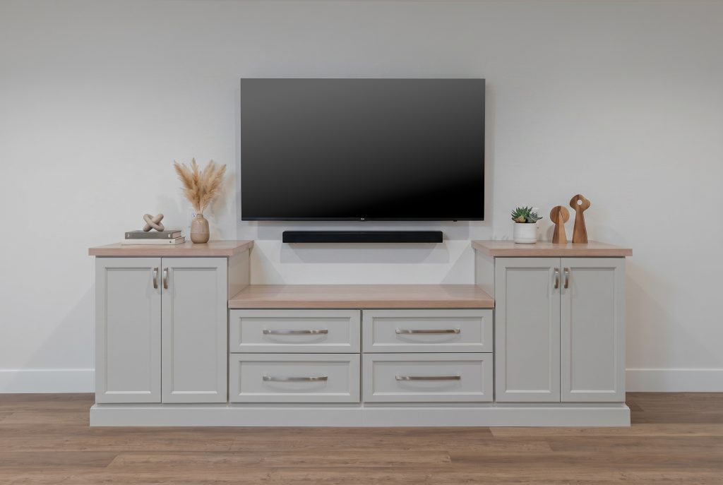 Mounted flat-screen TV above a slim black soundbar on a gray media console with decorative items on both sides of the cabinet.