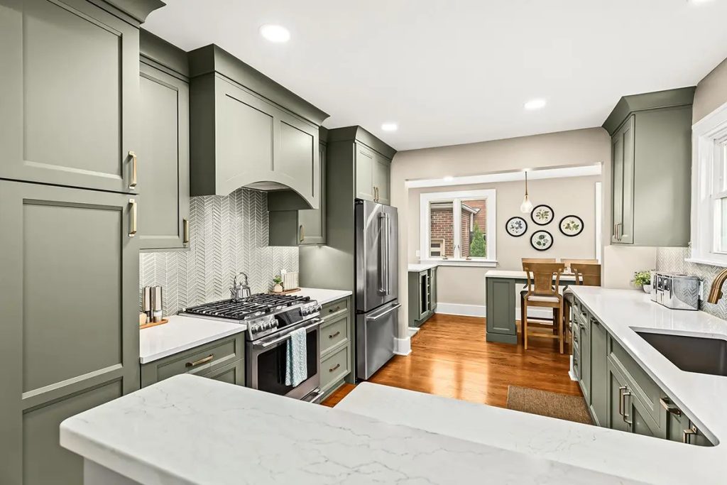 Modern kitchen with sage green cabinets, marble countertops, and stainless steel fridge and range with a herringbone backsplash.