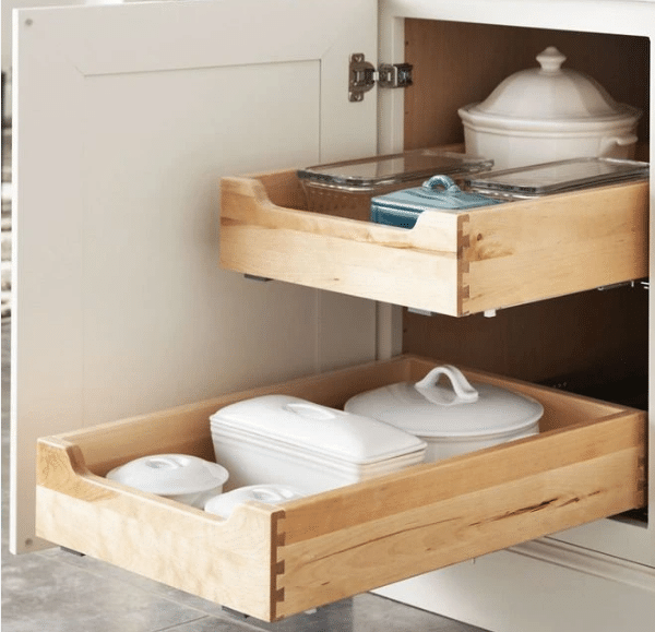 Screenshot 2026-09-24 140132 Open kitchen base cabinet with two wooden pull-out drawers storing white ceramic cookware and lids.